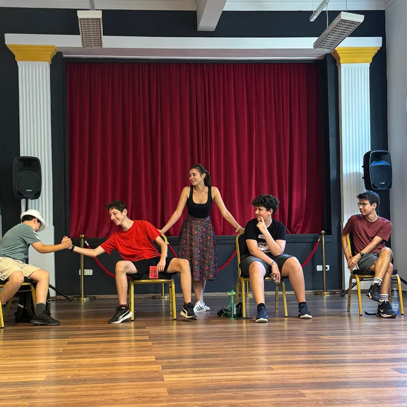 Adolescenți pe scenă, la o repetiție, în fața cortinei roșii Adolescenți pe scenă, la o repetiție, în fața cortinei roșii